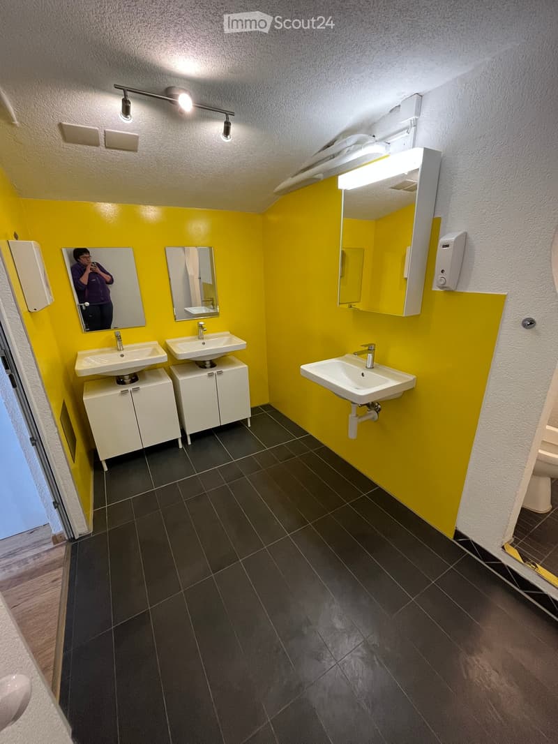 Bright yellow-walled bathroom with three white sinks, mirrors, and cabinets, featuring modern fixtures and dark tiled flooring.