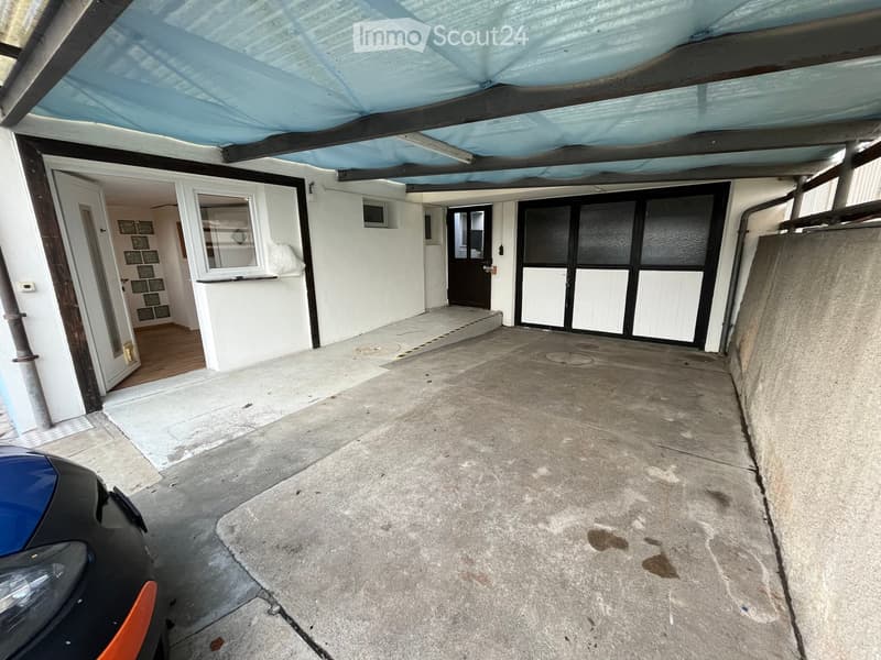 {"type": "Garage", "objects": [], "description": "Carport with concrete floor, covered roof, and access to a house with white walls and wooden flooring visible through an open door.", "localized_descriptions": {"EN": "Carport with concrete floor, covered