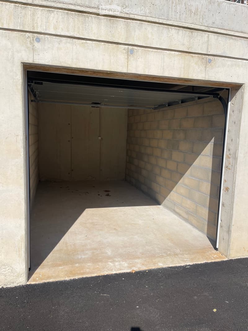 Open garage with concrete walls and a brick interior wall, featuring a raised ground floor and a concrete floor.