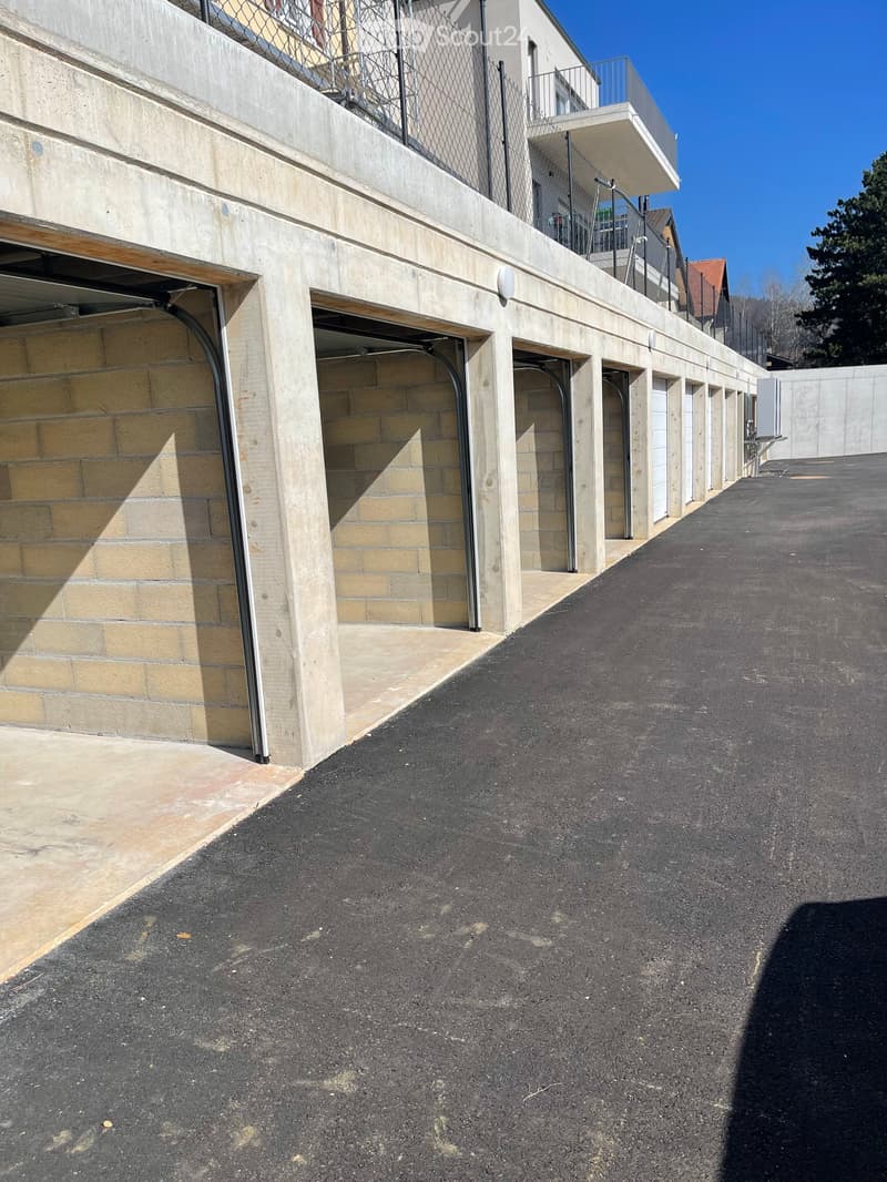 A row of modern garage entrances with concrete walls and metal doors, leading to a paved driveway.