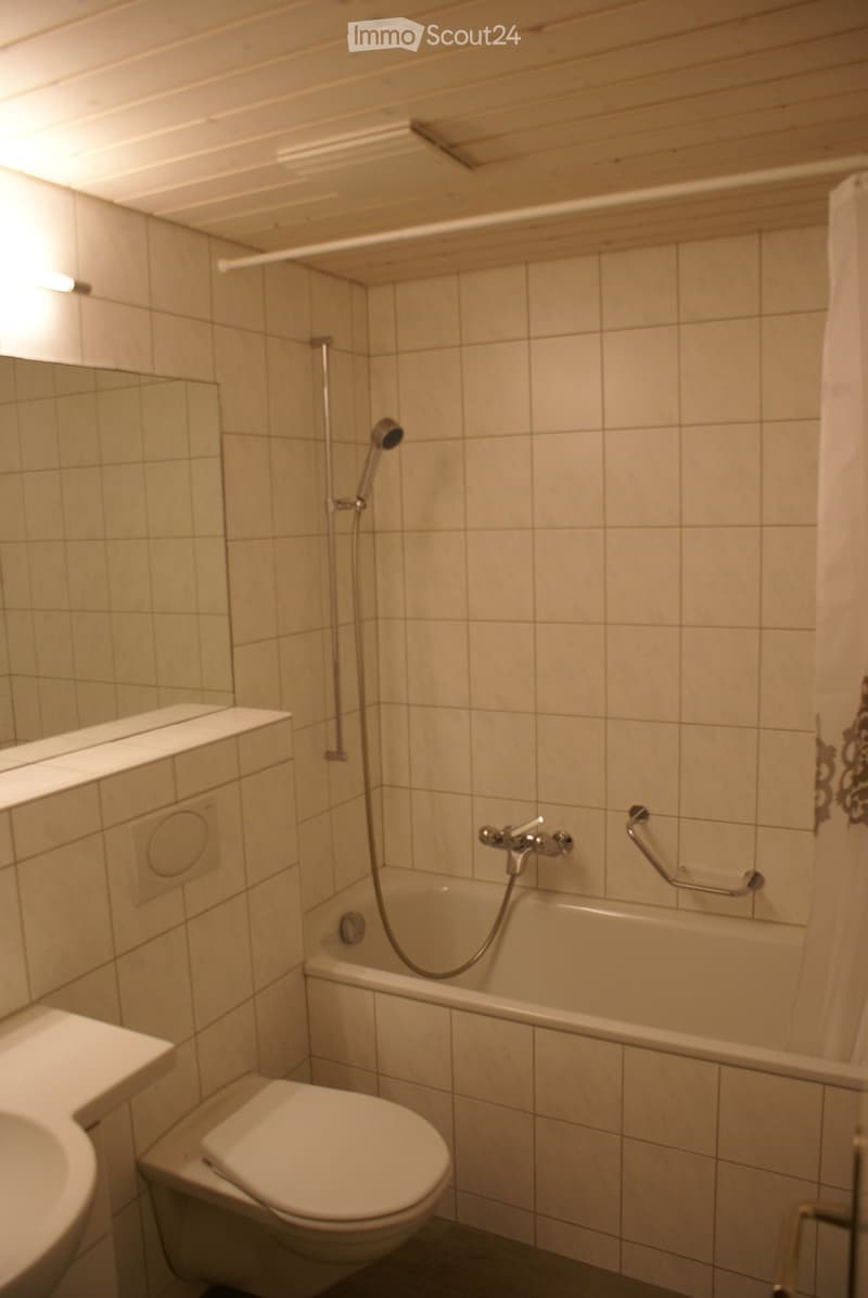 Bathroom with white tiles, a toilet, a sink, and a bathtub with a shower head and handle.