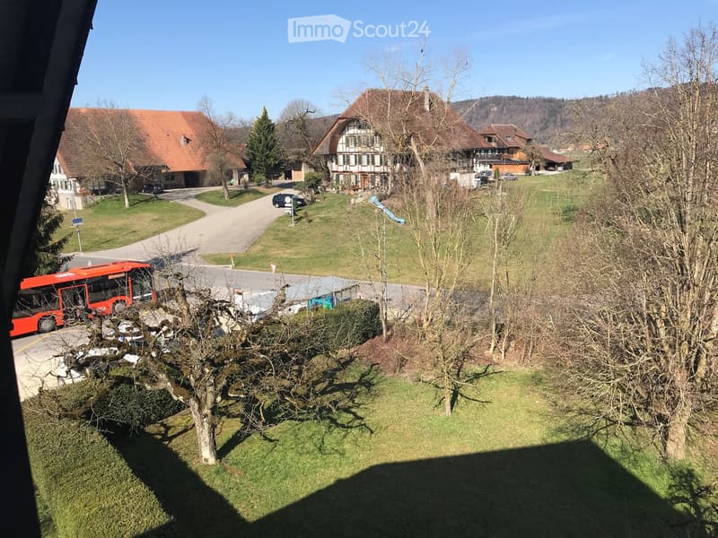 View from a balcony showing a rural village with houses, a bus, and a road leading to the village.