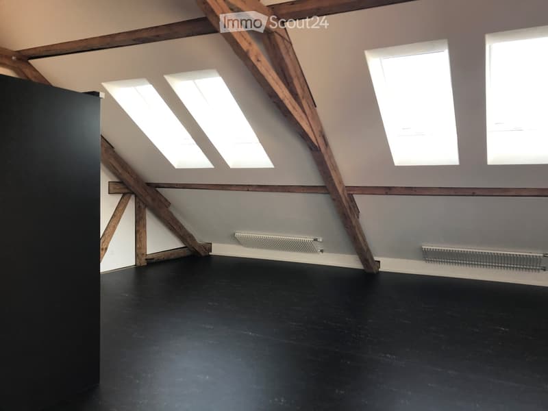 An empty attic space with exposed wooden beams, skylights, and a dark floor. No furniture or equipment is present.
