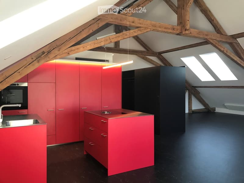 Modern kitchen with red and black cabinets, stainless steel sink, and exposed wooden beams on the ceiling.