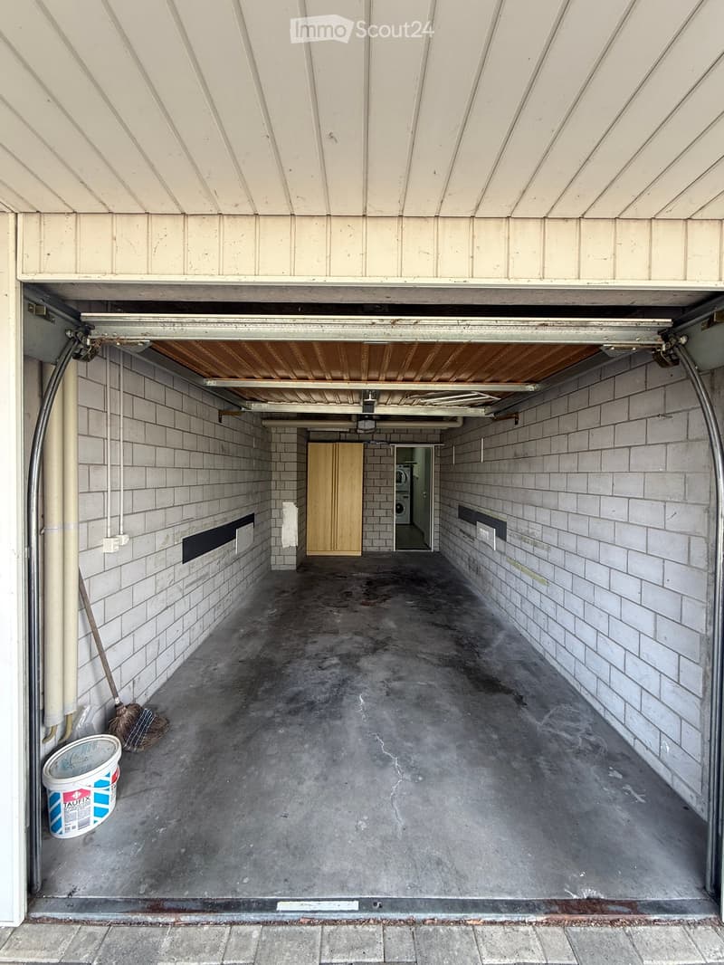 Empty garage with concrete floor, brick walls, and a wooden cabinet in the background.