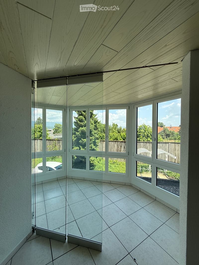 Empty room with large windows, wooden ceiling, and tiled floor. No furniture or equipment present.
