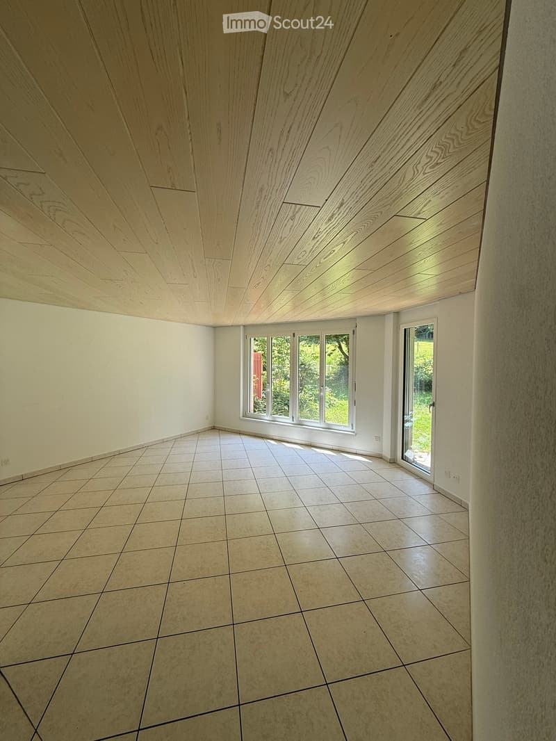 Empty room with tiled floor, white walls, and large windows, including a sliding glass door leading outside.