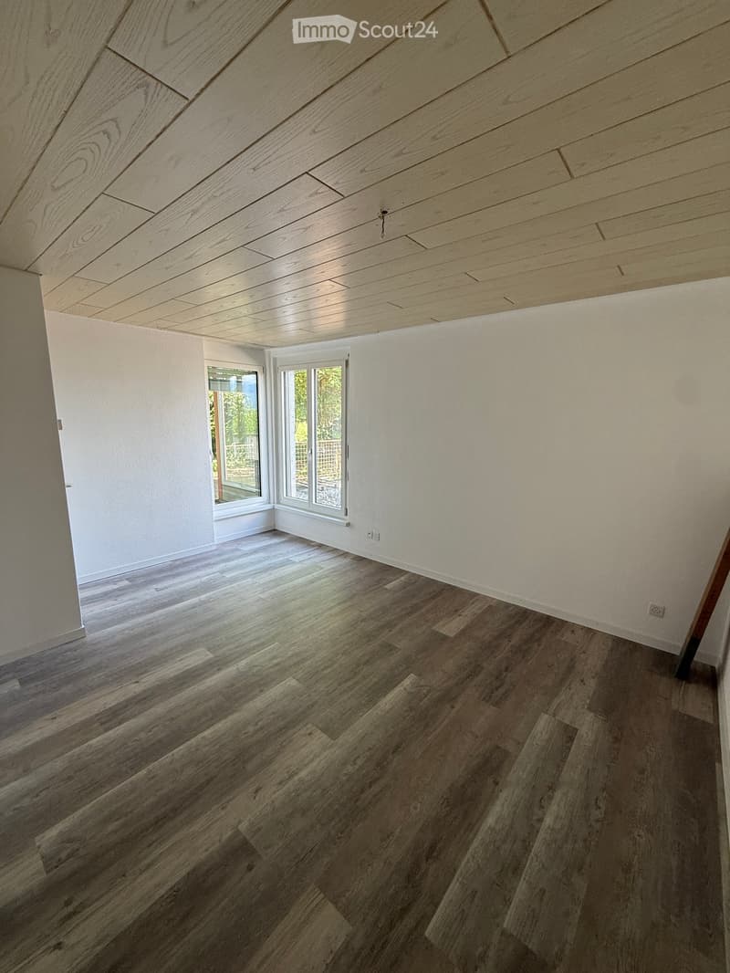 Empty room with wooden flooring and white walls, featuring large windows and a sliding glass door leading to an outdoor area.