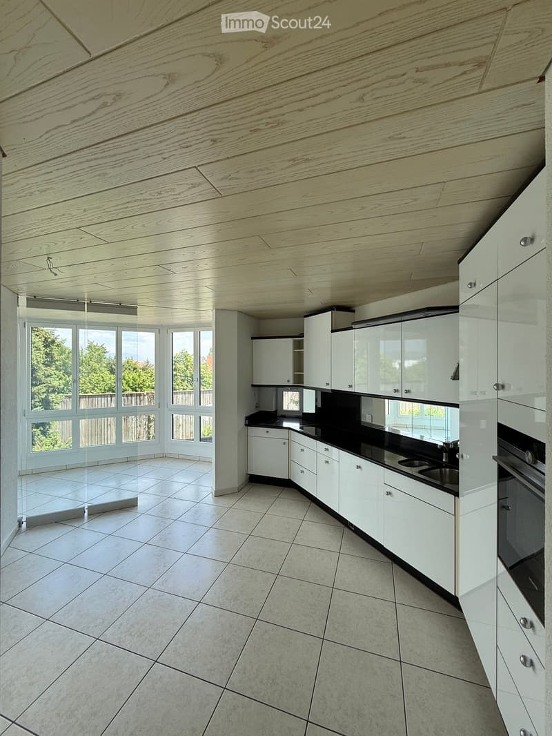 Modern kitchen with white cabinets, black countertops, and large windows overlooking a green area.