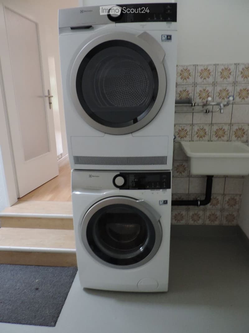 Bathroom with a stacked washing machine and dryer, tiled walls, and a small sink area.