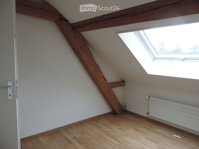 Empty attic room with wooden beams, wooden floor, skylight window, and radiator.