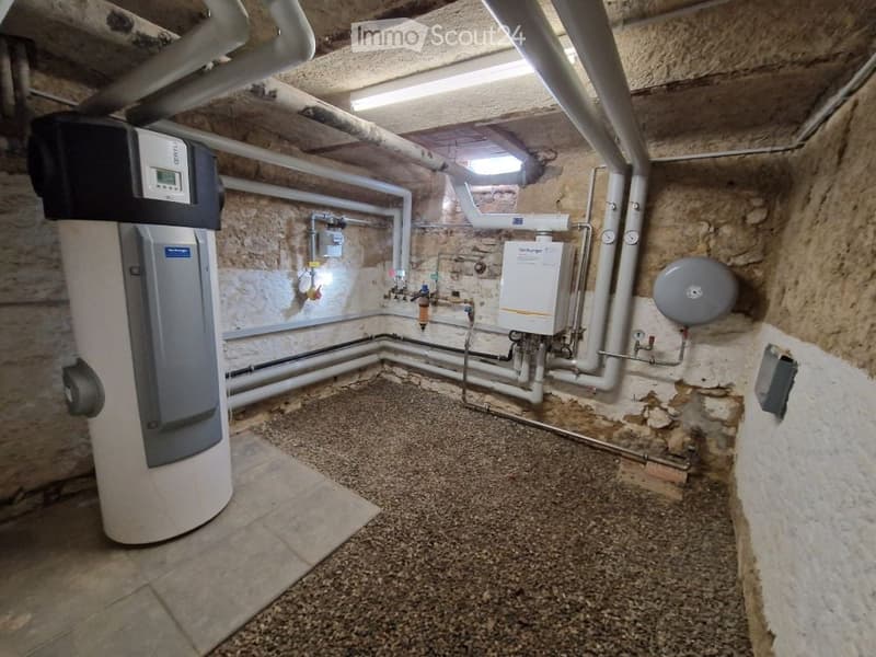 Utility room with exposed stone walls, water heater, boiler, and various pipes and valves.