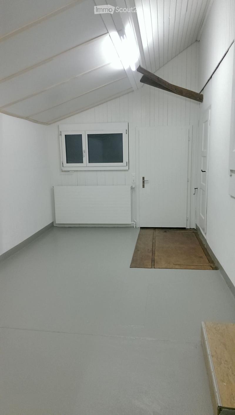 Empty room with white walls, grey floor, a window, a door, and a radiator.