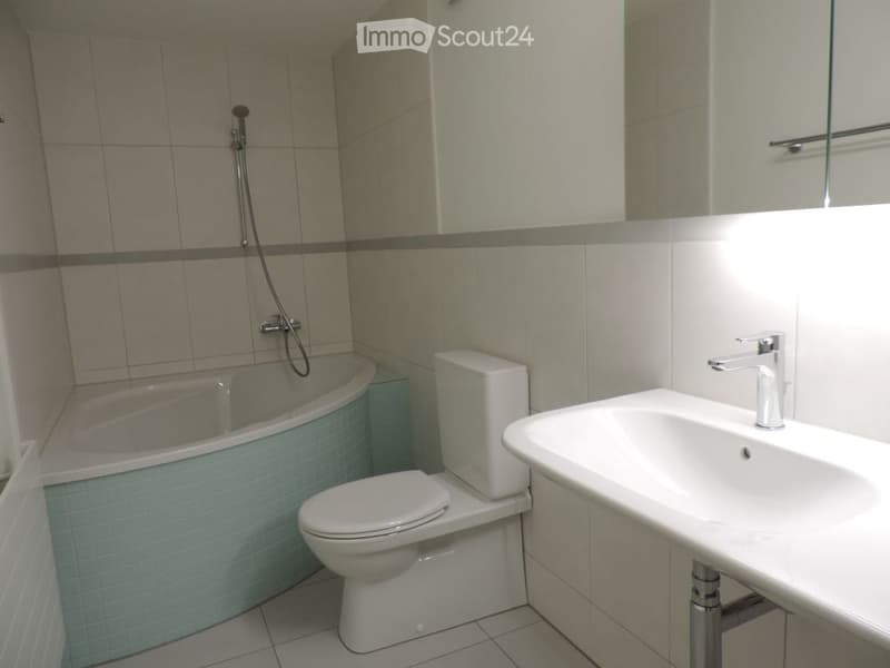 Modern bathroom with a bathtub, toilet, sink, and mirror. The walls are tiled in neutral tones, and the fixtures are sleek and contemporary.