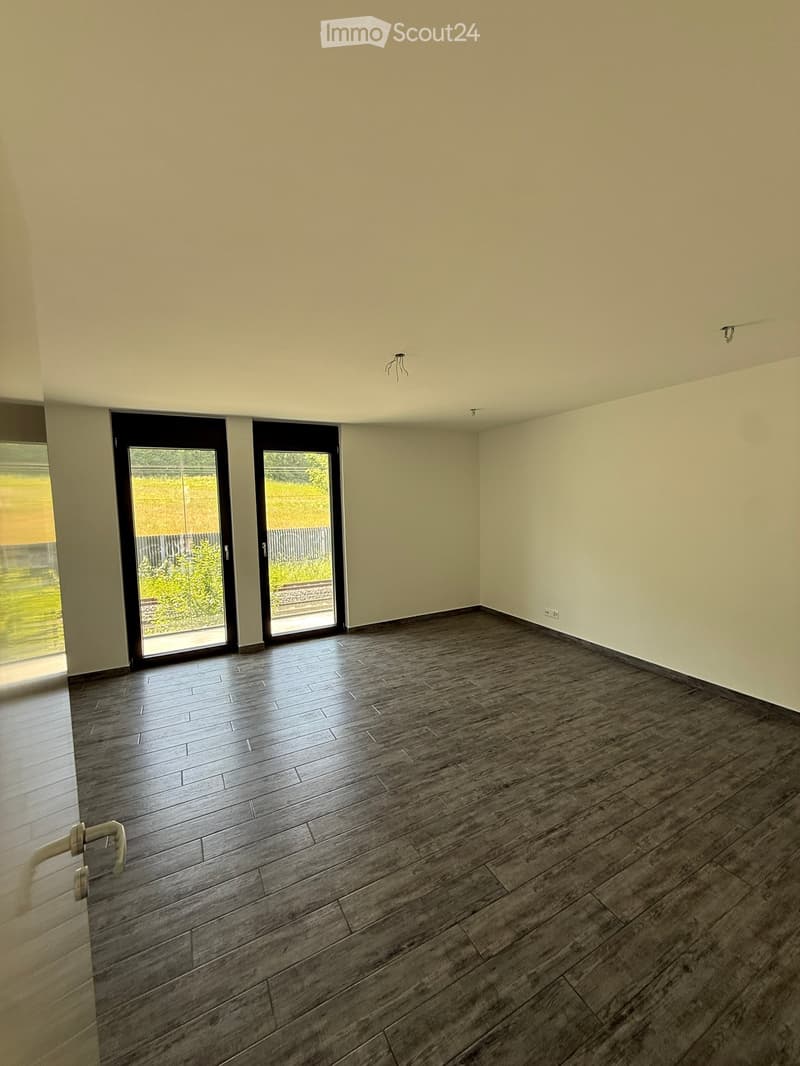Empty room with light-colored walls, dark wooden flooring, and large sliding glass doors leading to an outdoor area.