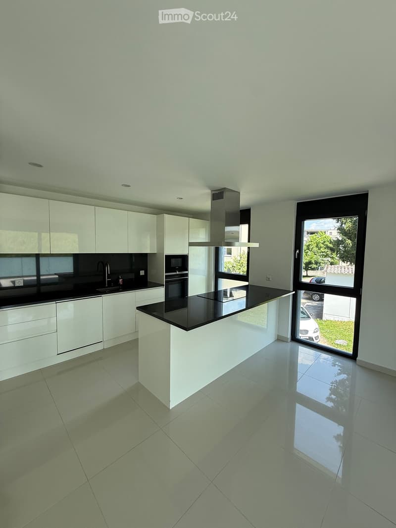 Modern kitchen with white cabinetry, black countertops, island, and stainless steel appliances.
