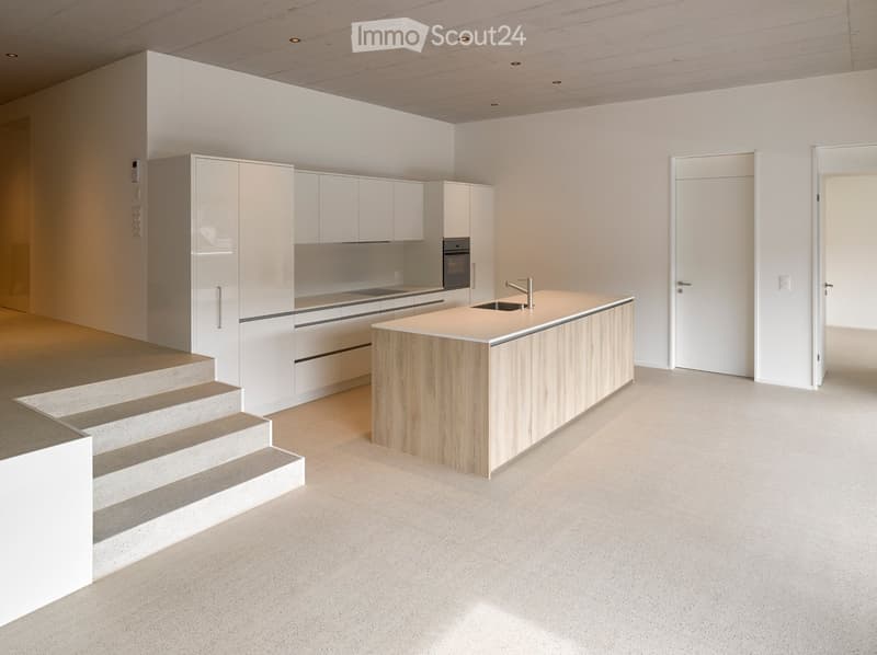 Modern, minimalist kitchen with white cabinetry, a central wooden island, and built-in appliances.