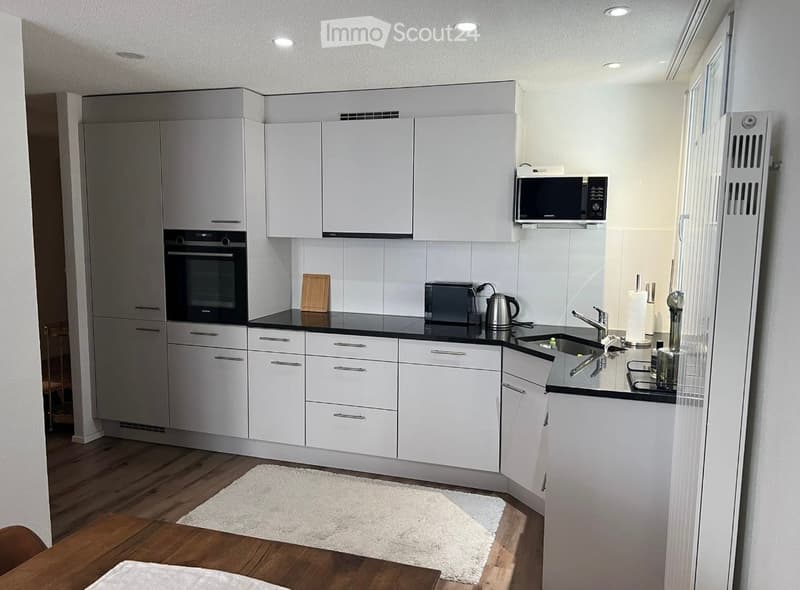 Kitchen. Modern kitchen with white cabinets, black countertops, stainless steel appliances, and a small wooden dining table.