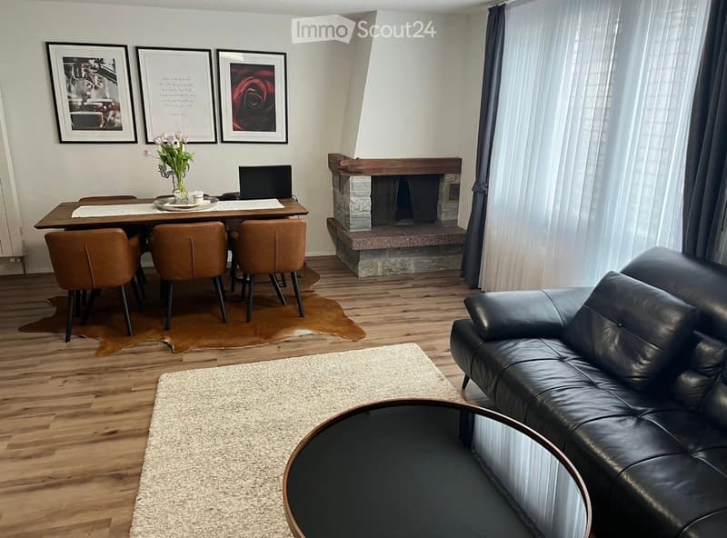 Furnished Room. Modern living and dining area with a black leather sofa, round coffee table, dining table with four chairs, fireplace, and artwork on the wall.