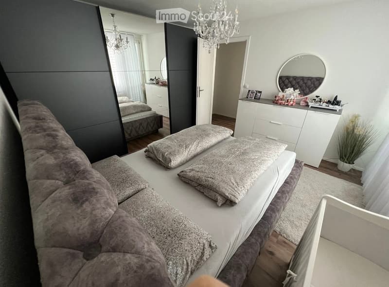 Bedroom. Modern bedroom with a large bed, multiple pillows, a wardrobe, a dresser with a mirror, and a chandelier hanging from the ceiling.