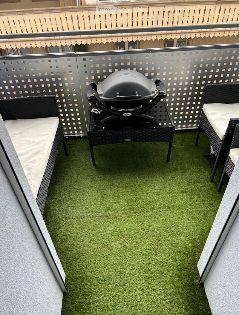 Balcony / Terrace. Balcony with artificial grass flooring, a black grill on a table, and two wicker chairs with white cushions.