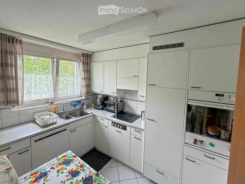 Modern kitchen with white cabinets, stainless steel appliances, and a window with curtains. Includes a sink, dishwasher, oven, refrigerator, microwave, and coffee maker.