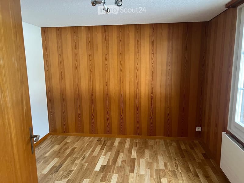Empty room with wooden walls and floor, white ceiling, and a window on one side.