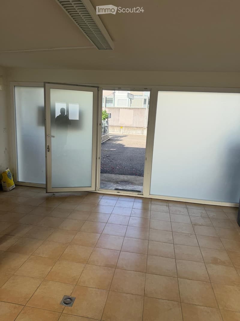 Empty room with tiled floor, large sliding glass doors leading to an outdoor area, and a small vent on the floor.