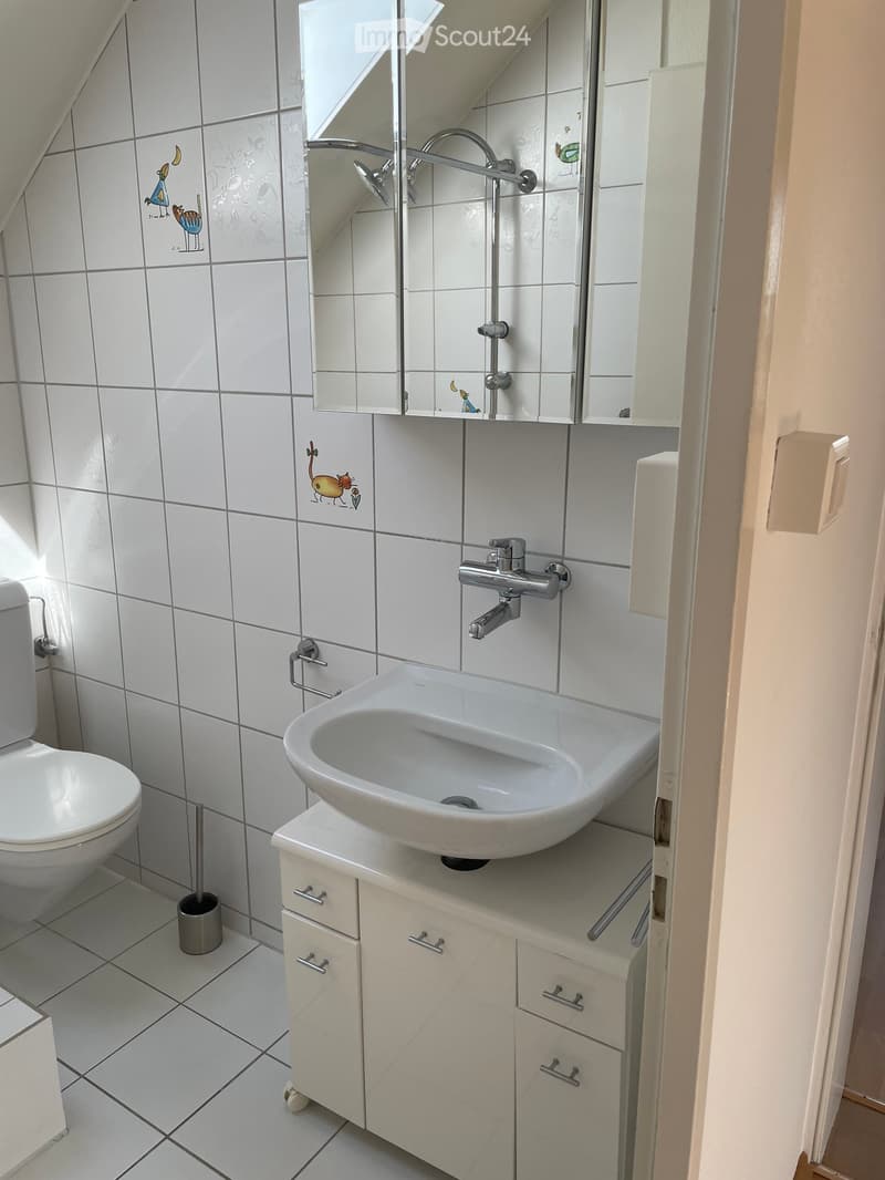 Clean bathroom with white tiles, a sink, toilet, mirror, and cabinet.