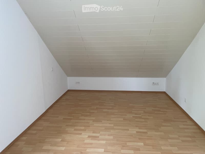 Empty room with light wooden flooring and white walls, featuring a white drop ceiling and electrical outlets.