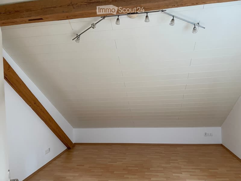 Empty room with wooden flooring, white walls, and a slanted ceiling with recessed lighting.
