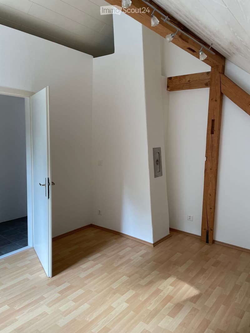 Empty attic room with wooden floor, white walls, exposed wooden beams, and a single door leading to another space.