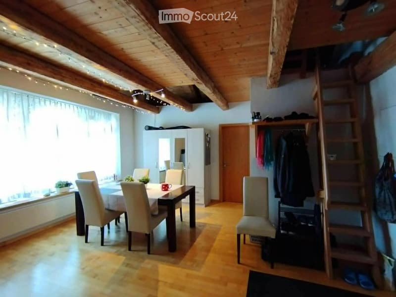 Bright, wooden-floored room with a dining table and chairs, a wardrobe, and a staircase leading to a loft area.