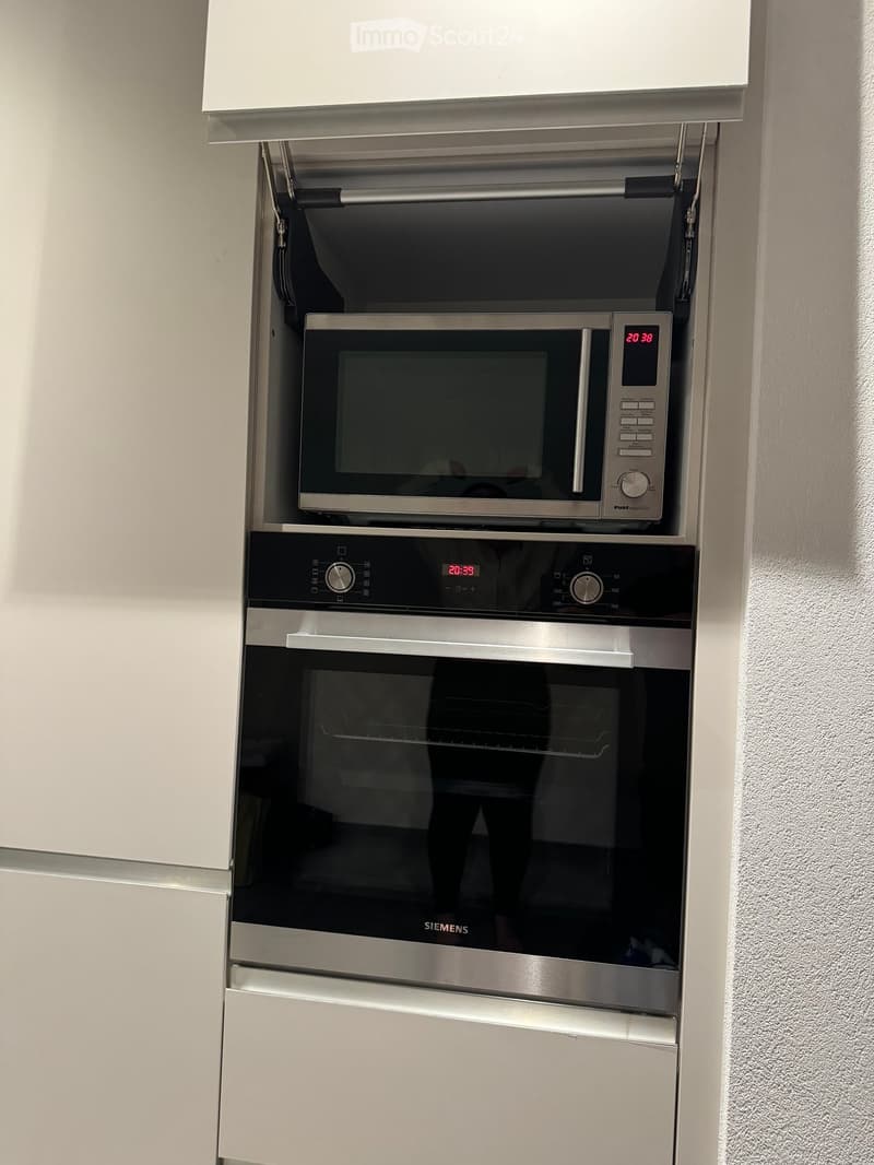Modern kitchen with built-in microwave and oven, sleek stainless steel finish, digital displays showing time.
