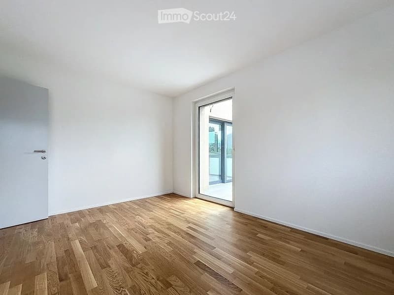 Empty room with light wooden flooring, white walls, and a large sliding glass door leading to a balcony.