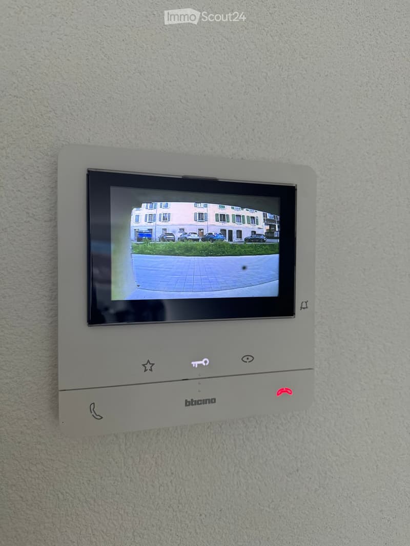 A wall-mounted security system with a screen displaying an outdoor view, featuring several control buttons and icons.