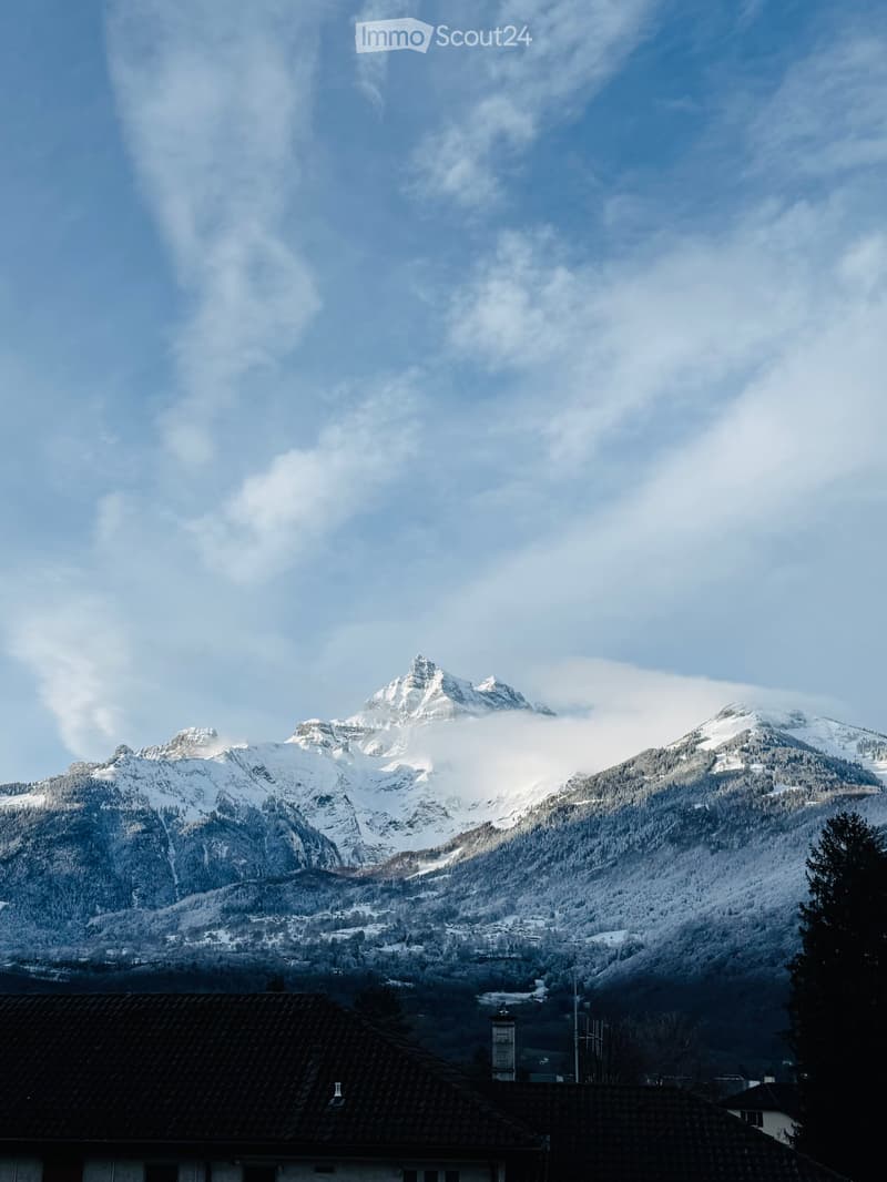 A view of a snow-covered mountain range with a small house in the foreground.