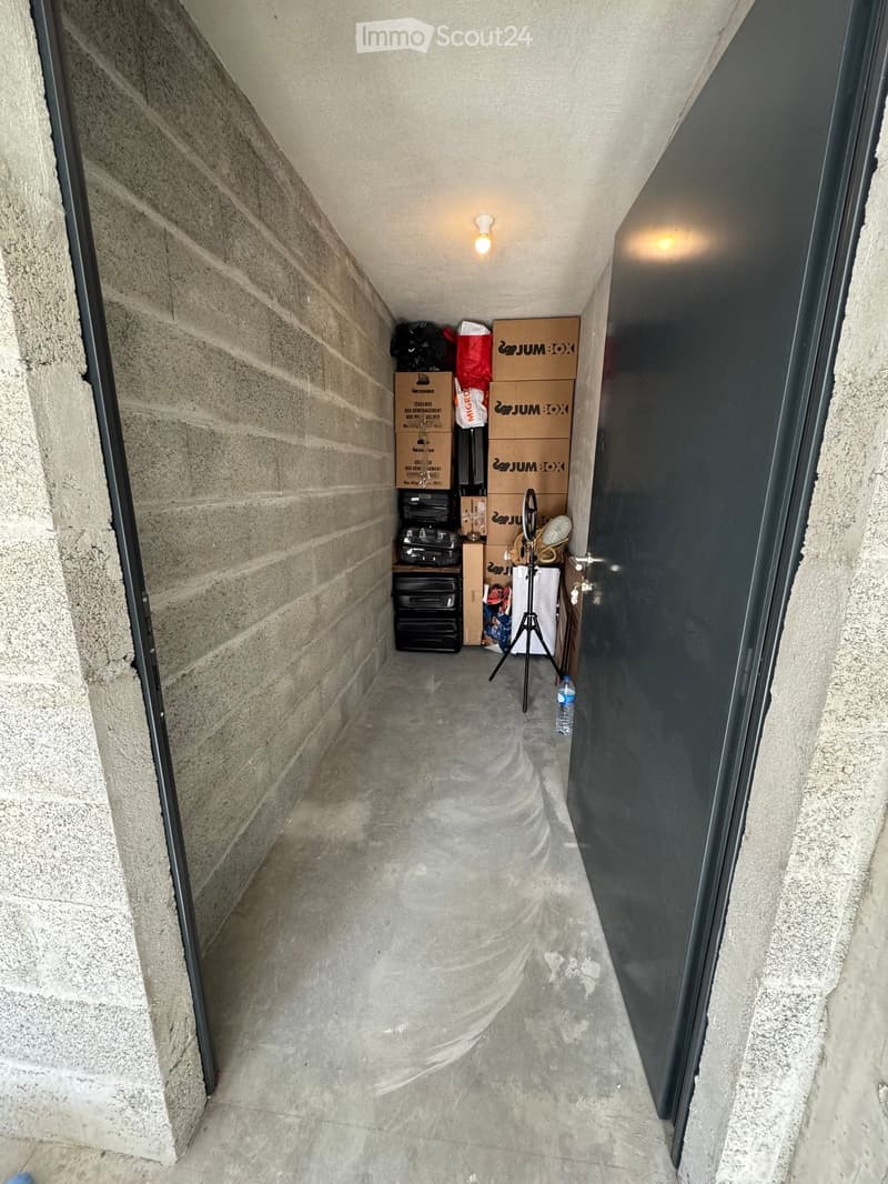 Narrow concrete hallway with storage boxes, a tripod, and a water bottle on the floor.