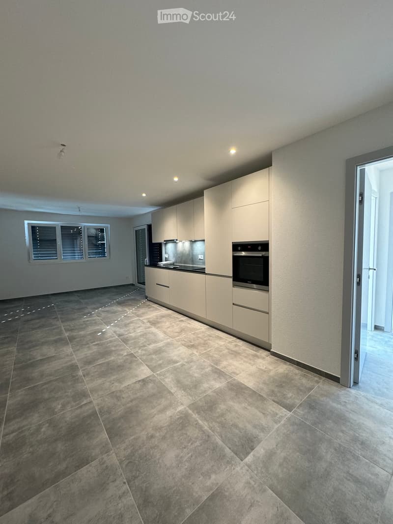 Modern kitchen with light-colored cabinets, stainless steel oven, and granite tile flooring.
