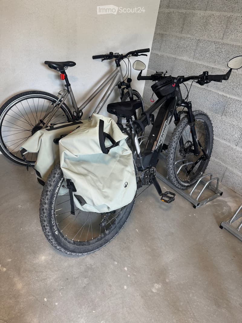Two bicycles with bags parked against a wall in a concrete area.