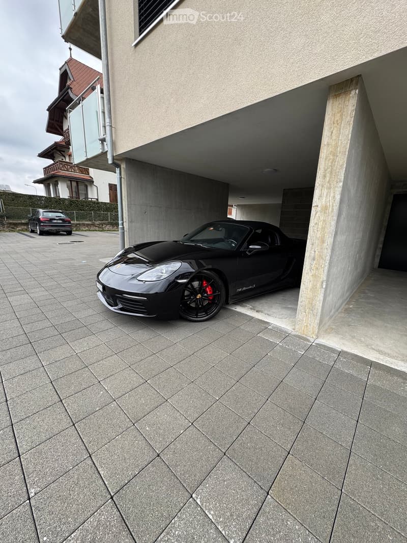 Modern building with a covered garage area, featuring a sleek black sports car parked inside and another car parked outside.