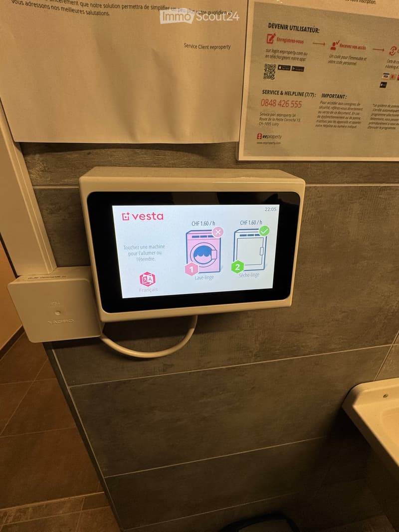 Bathroom with a wall-mounted screen displaying washing and drying machine options, a sink, and informational posters on the wall.