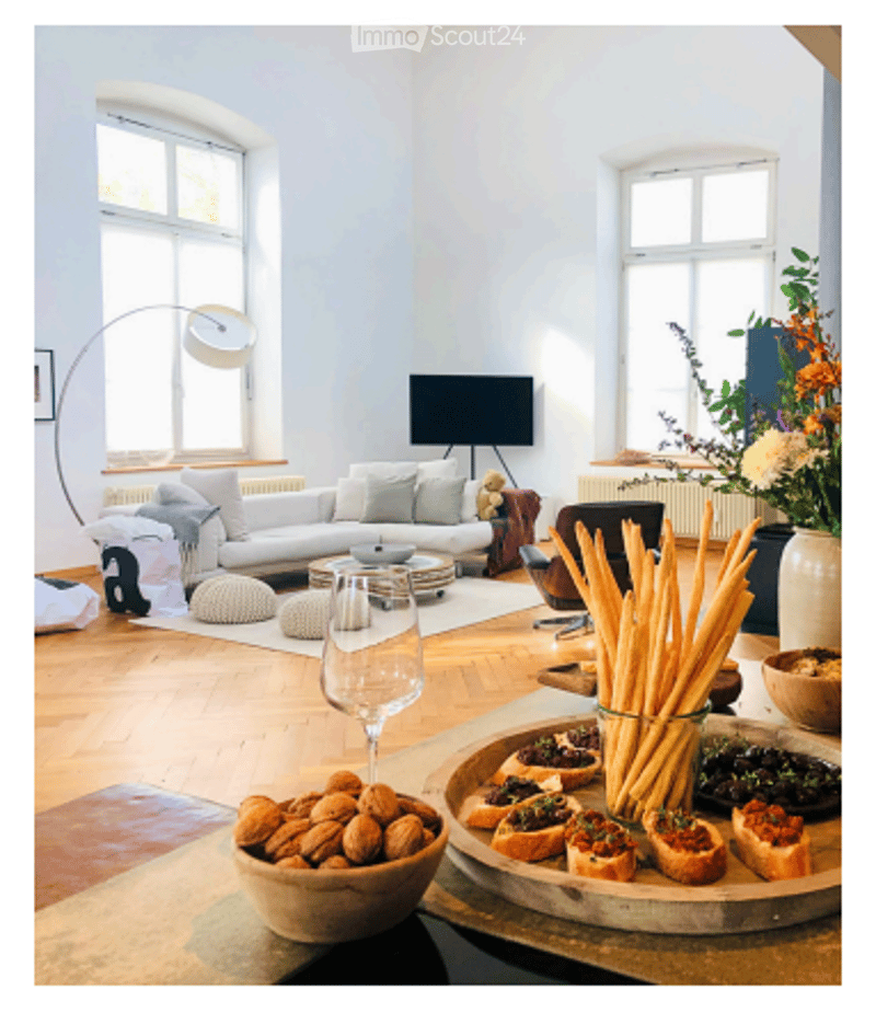Bright living room with large windows, white walls, grey sofa, coffee table, floor lamp, TV, and decorative items on the table.