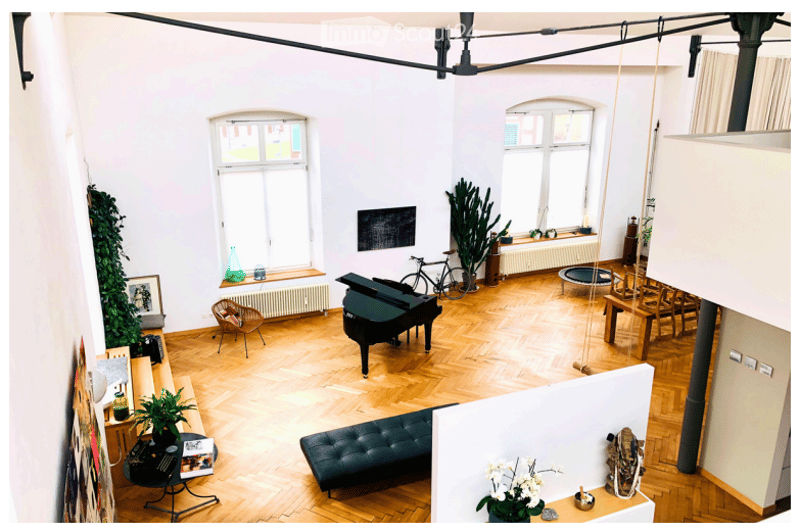 Open-plan living space with wooden flooring, large windows, a black piano, a sofa, a bicycle, and several plants.