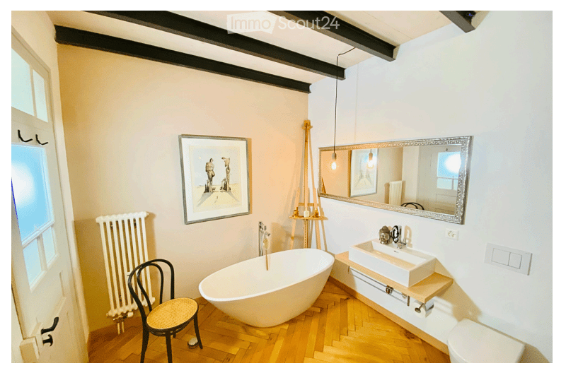 Bathroom with a freestanding bathtub, a modern sink, a wicker chair, a radiator, a large mirror, and a framed picture on the wall.