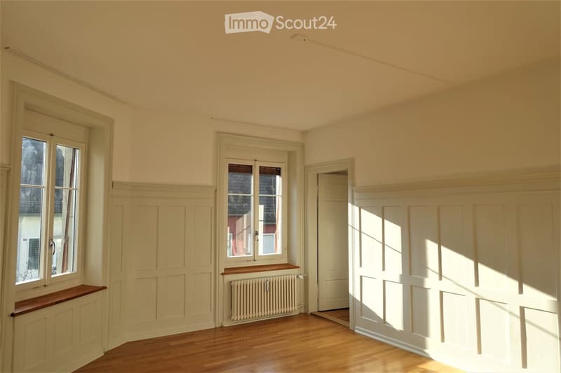 Empty room with wooden flooring, white walls, large windows, and a radiator. No furniture or equipment present.