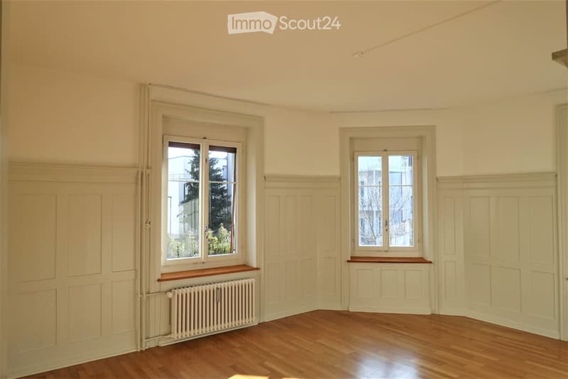 Empty room with wooden flooring, white walls, two windows with wooden sills, and a radiator under one window.