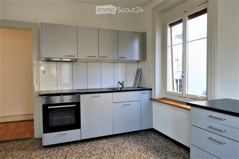 Modern kitchen with white cabinets, black countertops, stainless steel oven, sink, and faucet. Features large windows and wooden flooring.