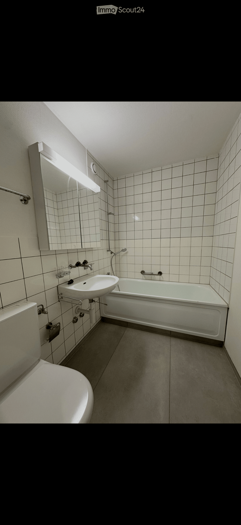 Modern bathroom with white tiled walls, a bathtub, a sink, a toilet, and a large mirror with built-in lighting.
