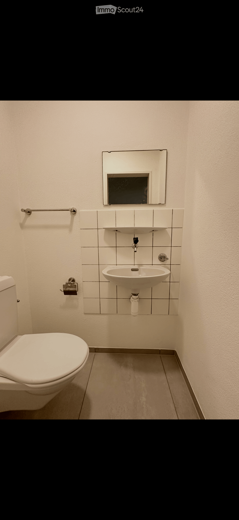 Modern bathroom with white tiled walls, a toilet, a sink with a mirror above it, and a towel rack on the wall.
